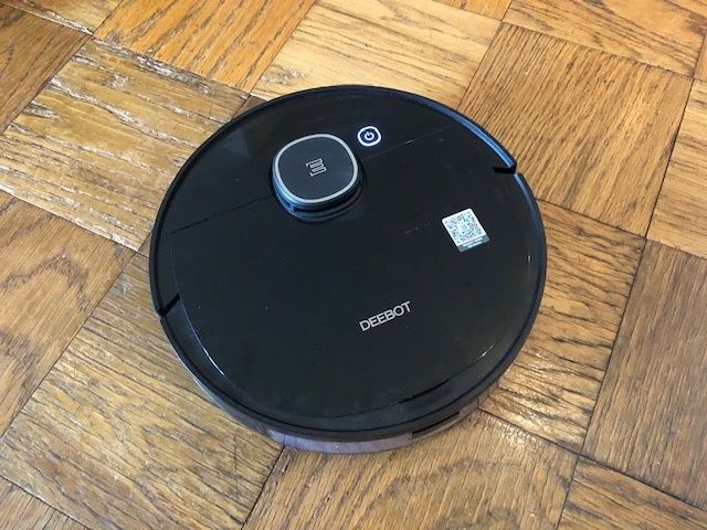 Round, black robot vacuum with the word "DEEBOT" on top on a wood floor