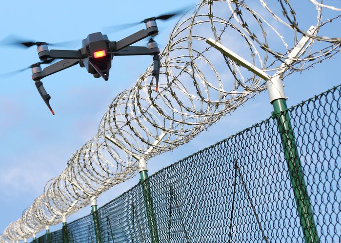 Drone with an orange light on the front, hovering over a barbed wire fence