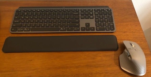 A keyboard, wrist pad, and silver mouse on a wooden table