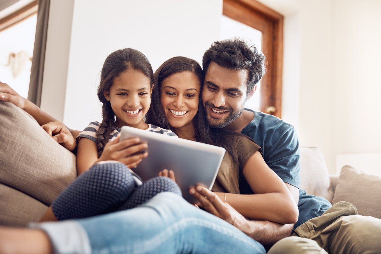 a family sitting on a sofa together looking at their tablet.