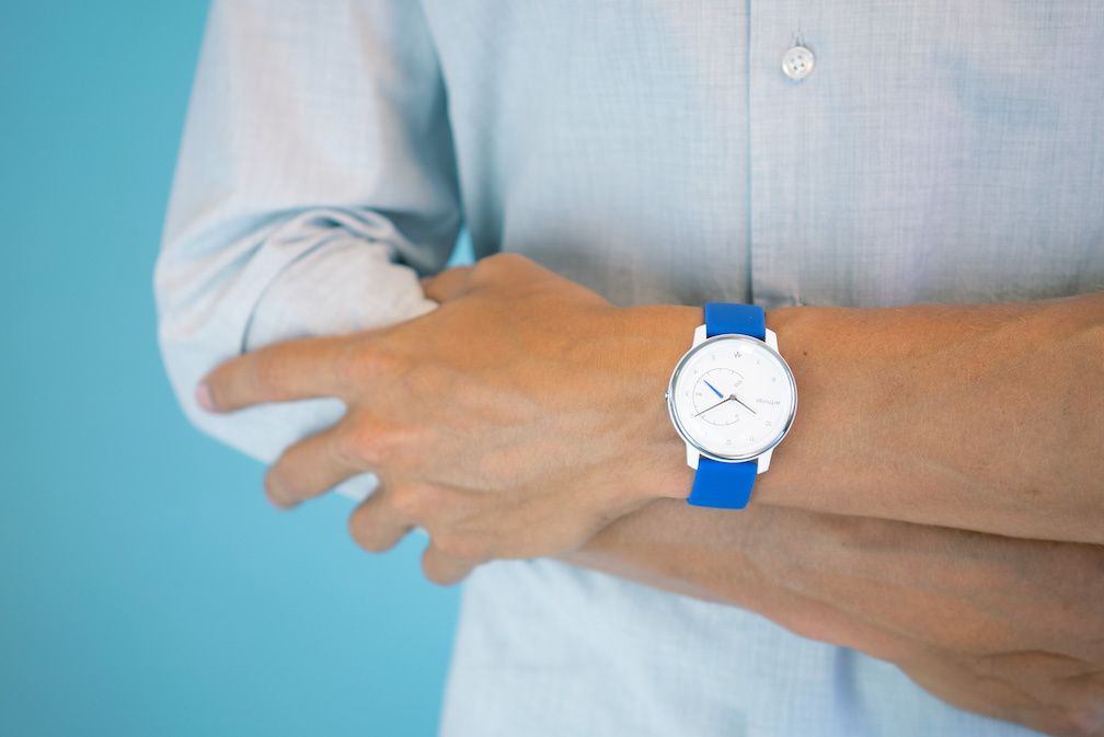 A watch with a blue band, white watch face, on an arm with shirt sleeves pushed back