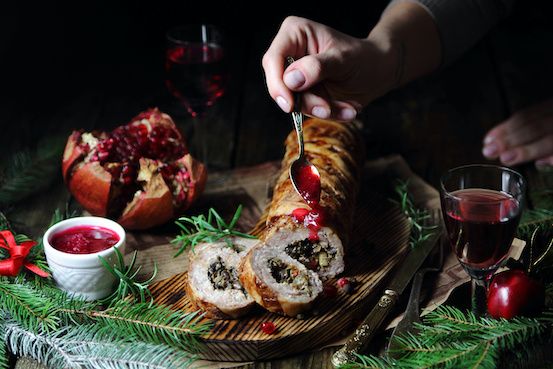 Festive food on a wooden tray surrounded by a glass of wine and pine branches