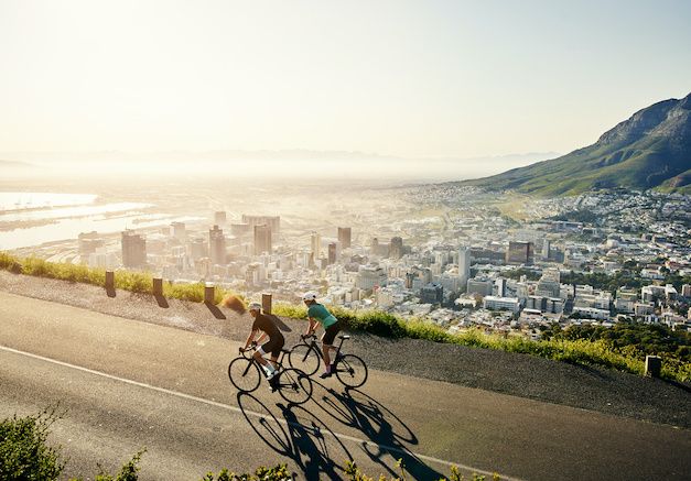 Two people riding bicycles on a highway above a city on a sunny day