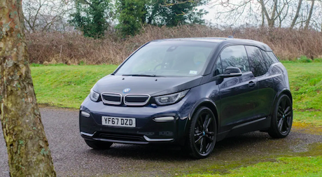 The BMW i3 electric car in black in a parking area surrounded by grass and trees