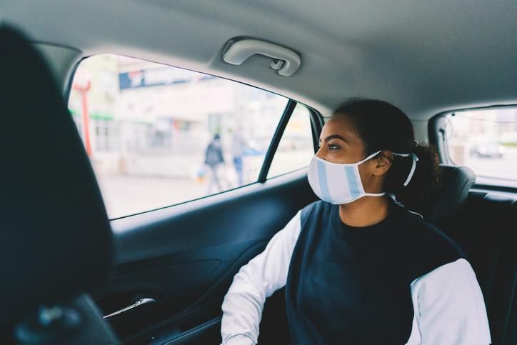 A rider in the back of a car, wearing a mask