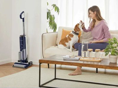 a woman sitting on a couch with her dog and a Tineco Dry Vacuum is in the corner.