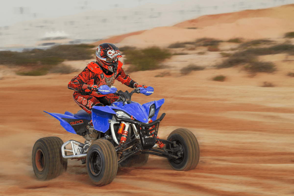 man-in-red-outfit-riding-an-atv-on-brown-sand