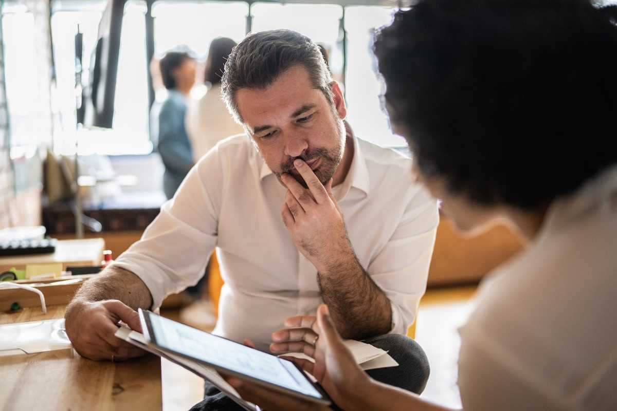 Mature man looking at a digital tablet that a colleague is showing at work stock photo