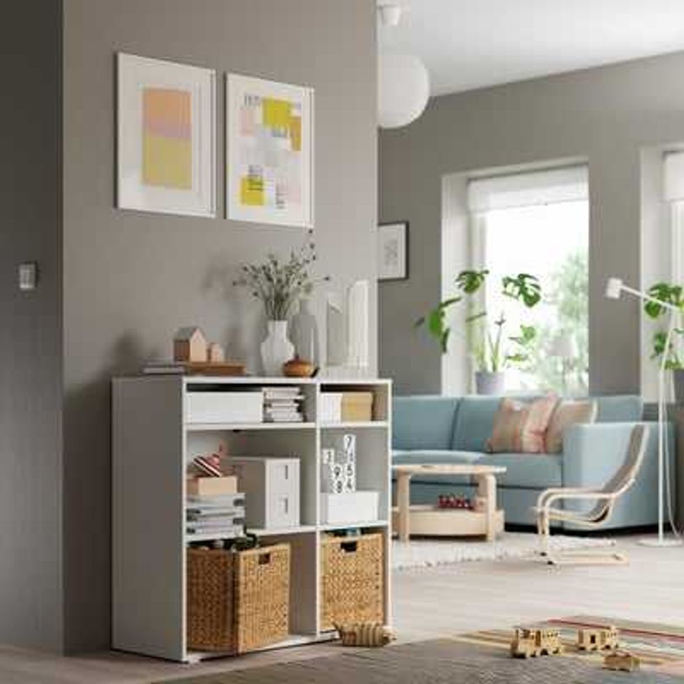 Modern living room with grey storage unit, wicker baskets, blue sofa, and artwork.