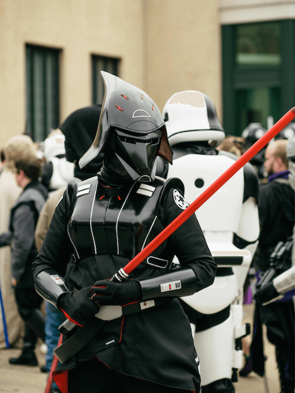 Person in Black Long Sleeve Costume and Black Helmet Holding Red Stick
