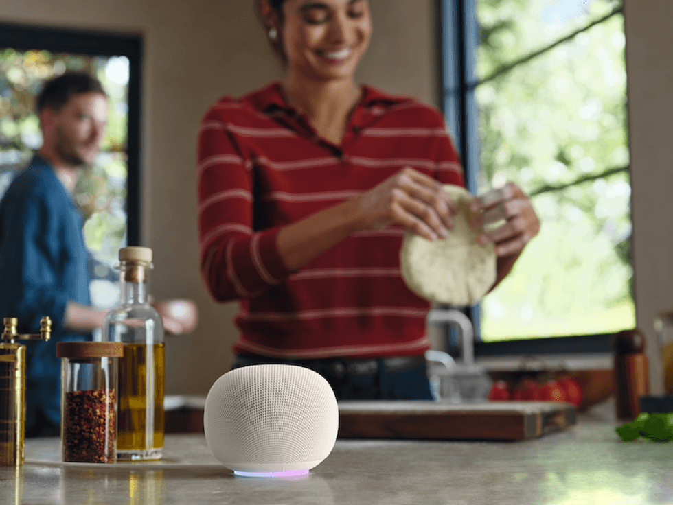 photo of Google Home Speaker on kitchen counter with a woman cooking in the background.