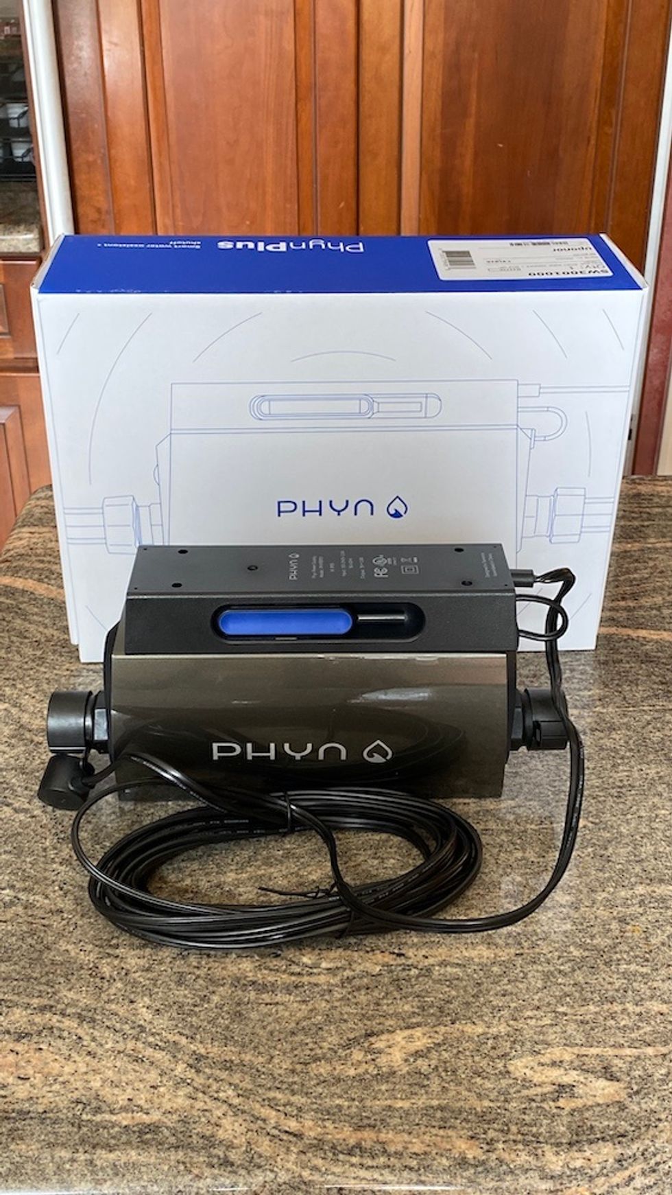 Photo of Phyn Plus smart water monitoring system on a counter in front of its box.