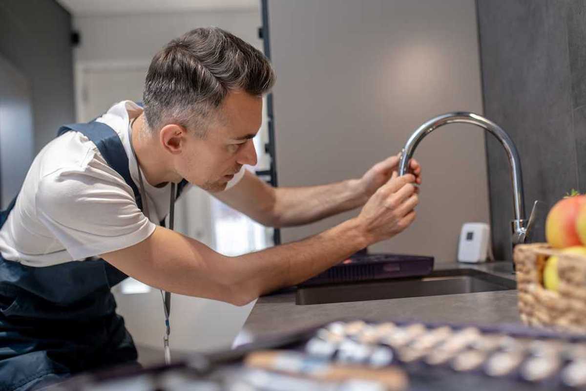 photo of Water tap prevention concentrated man leaning over water faucet touching spout pipe