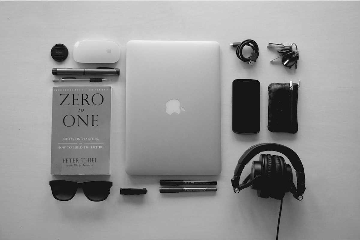 silver MacBook near black corded headphones and assorted items