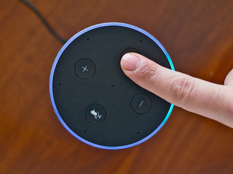 Someone putting their finger on the top of a smart speaker which is lit up with a blue rim