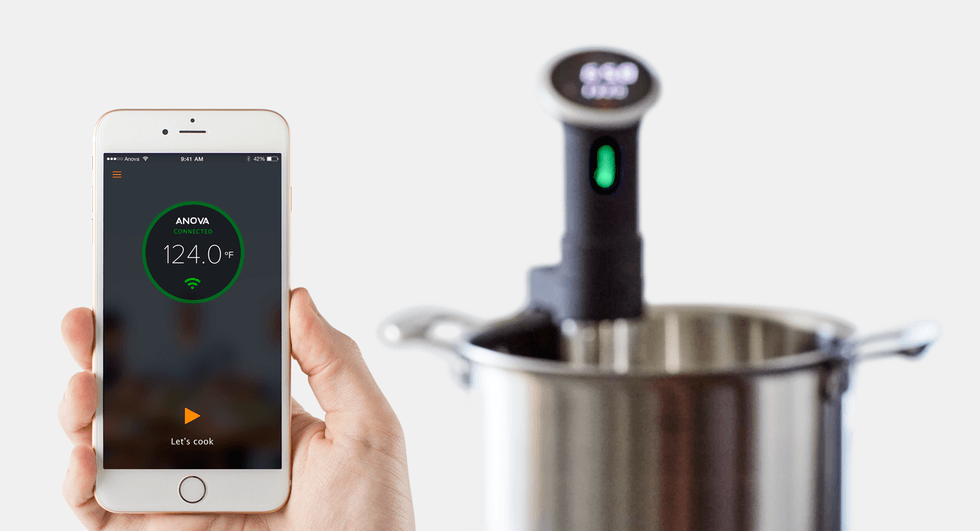 The Anova Sous Vide in a stainless pot next to a smartphone