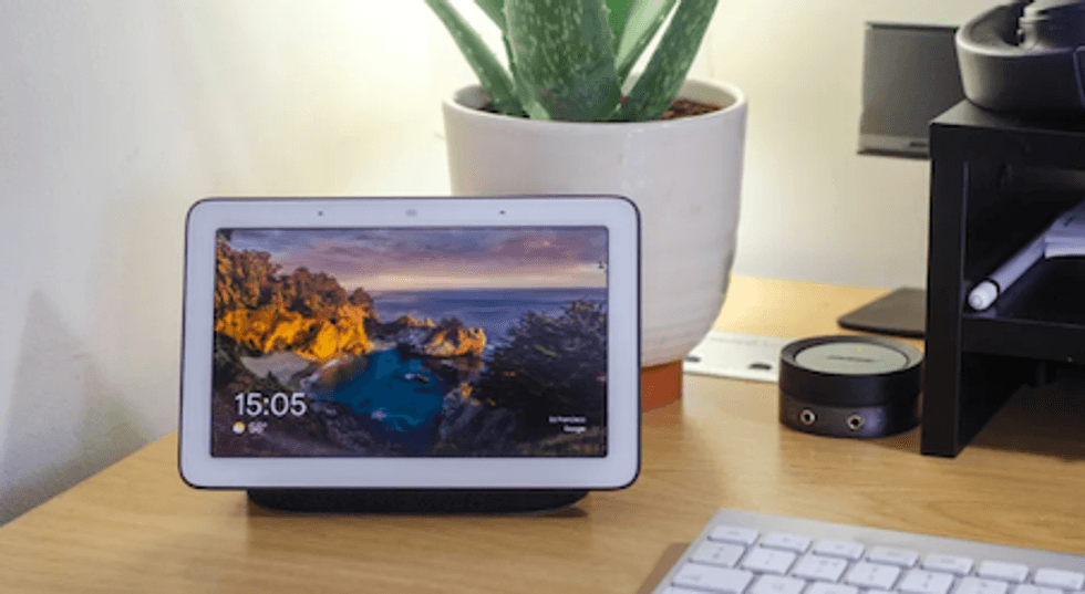 The Google Home Hub on a work desk next to a plant and keyboard