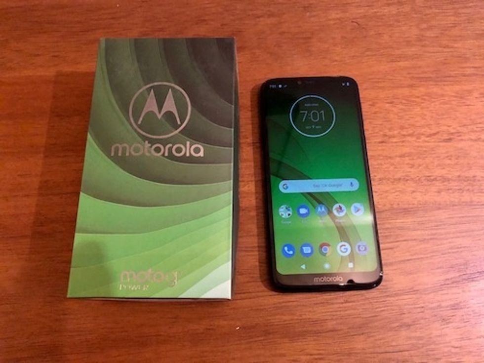 The Motorola Moto G7 smartphone next to its box on a wood table