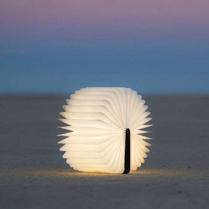 The Lumio Book Lamp opened into a pinwheel shape on a sandy beach