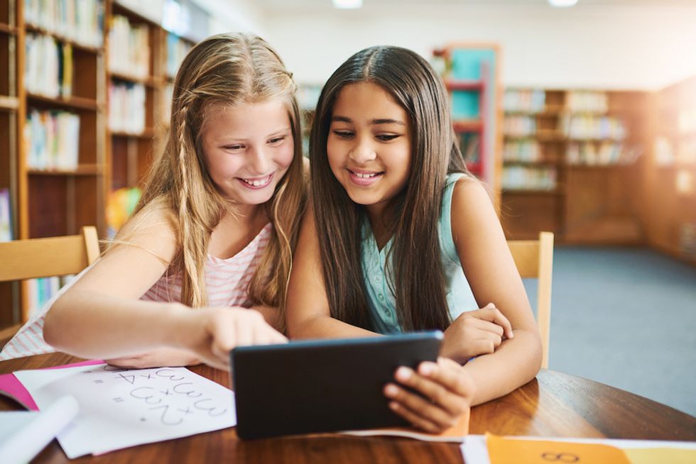 Two middle school students, smiling as they look over a tablet in a school library
