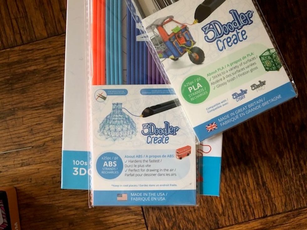 Two packages of plastic strands that read ABS and PLA on them in rainbow colors