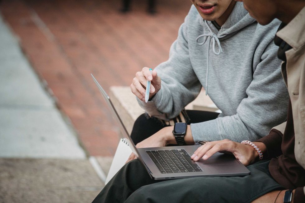Two students collaborate on a laptop outdoors for a university project. Focus on teamwork and digital learning.
