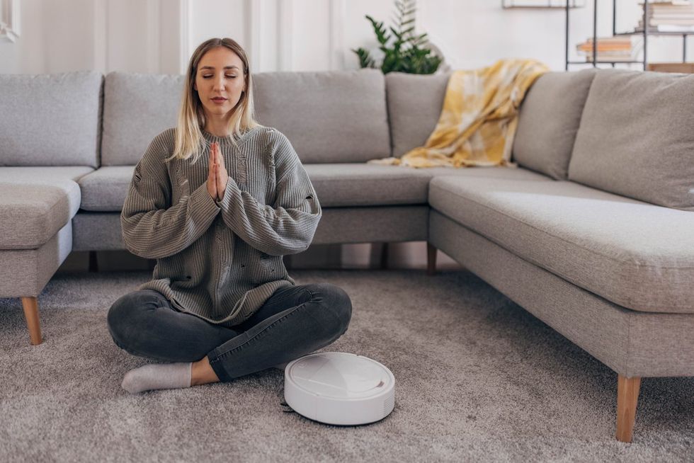 Woman meditating on the floor with a robot vacuum next top her cleaning stock photo